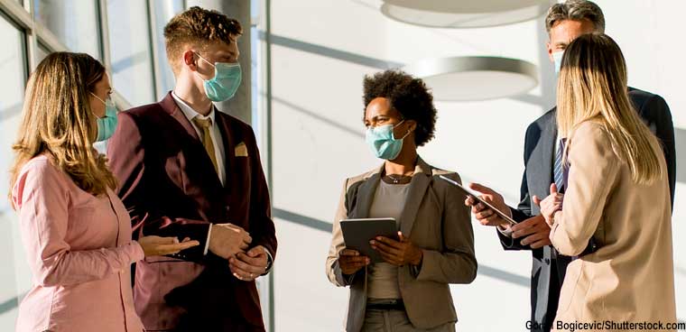 masked office workers talking in hallway (Goran Bogicevic/Shutterstock.com)